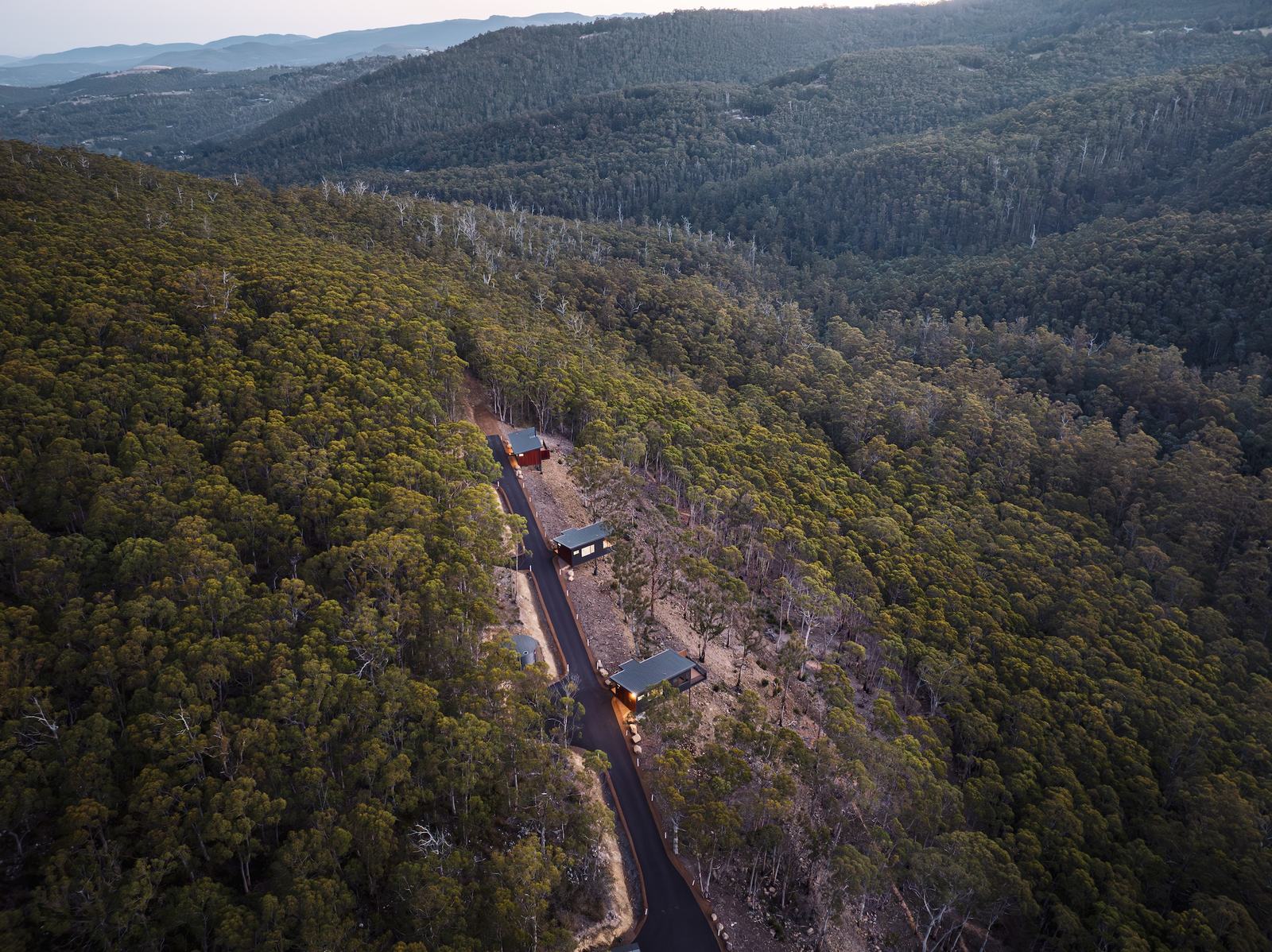 Three cabins lined up on the hillside overlooking a forest valley