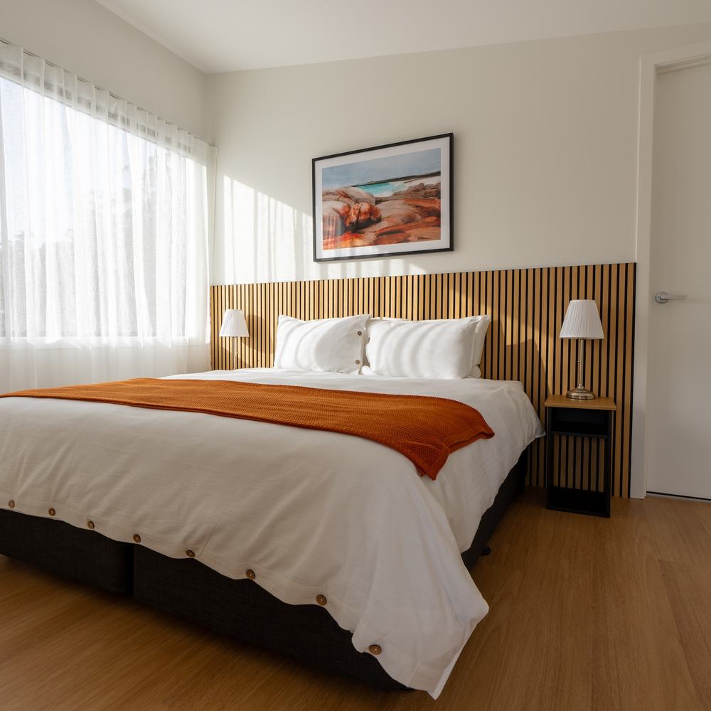 Full picture of ironbark bedroom showing bed soft curtains and artwork