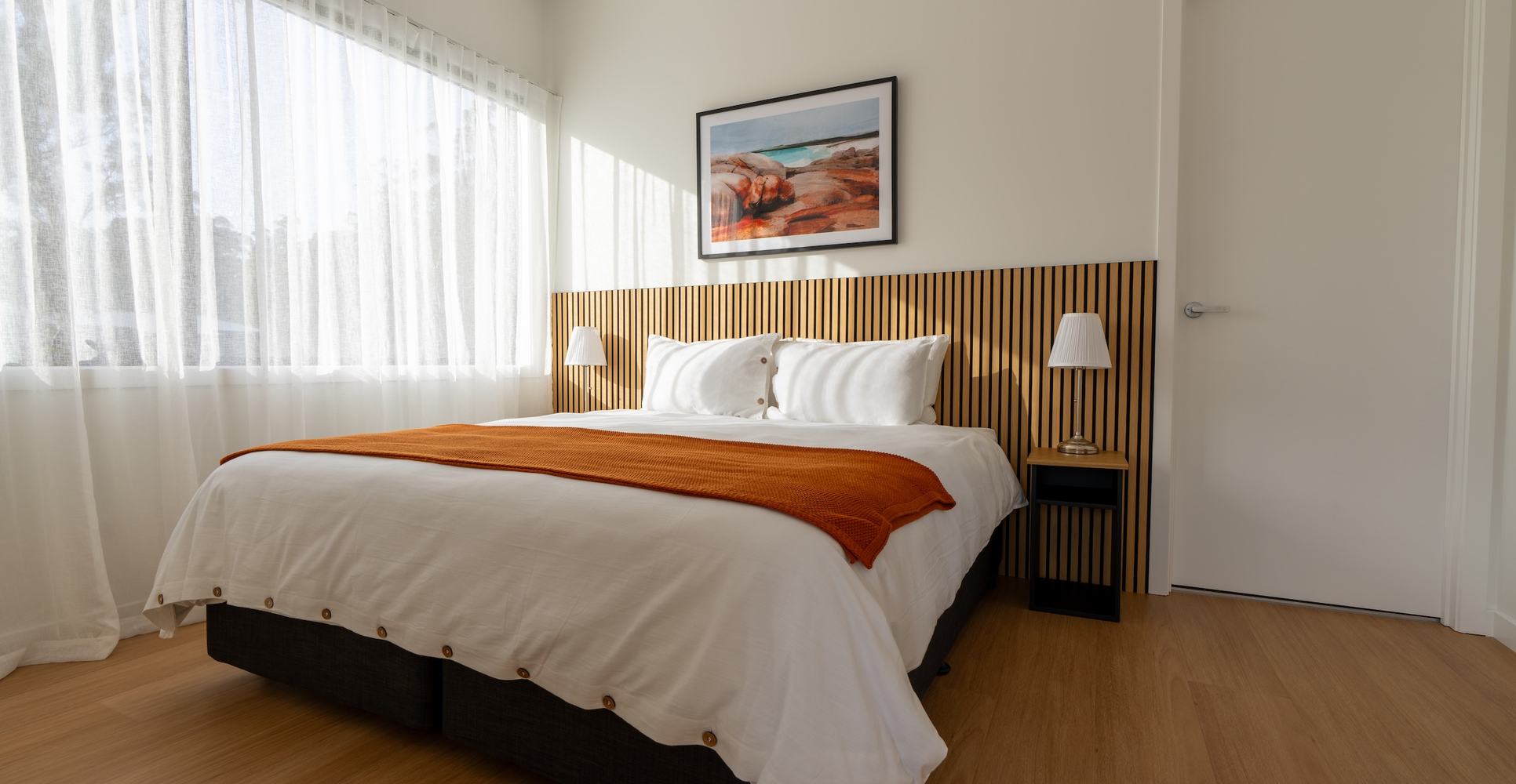 Full picture of ironbark bedroom showing bed soft curtains and artwork