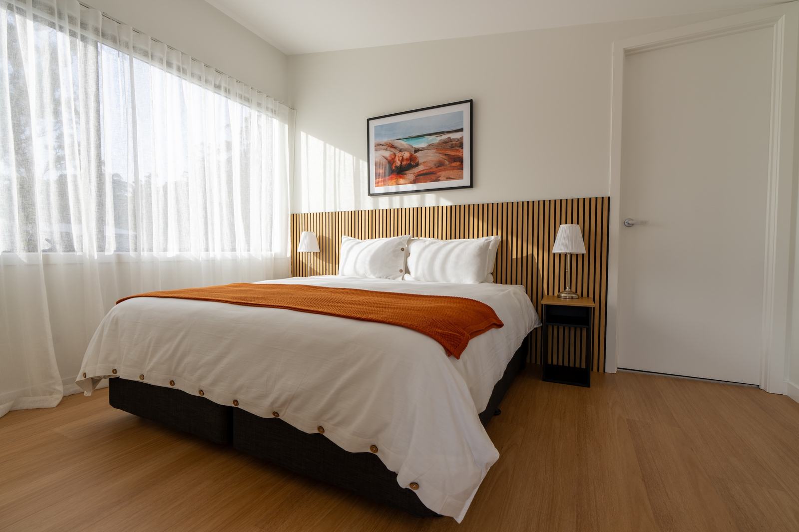 Full picture of ironbark bedroom showing bed soft curtains and artwork