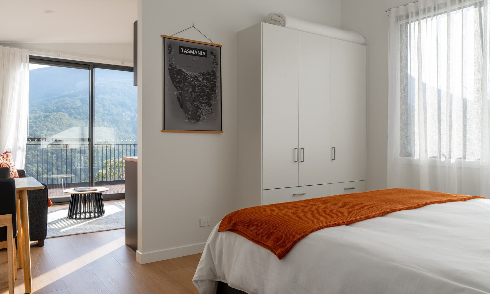 Bedroom of ironbark cabin looking to lounge room with mountain views through windows