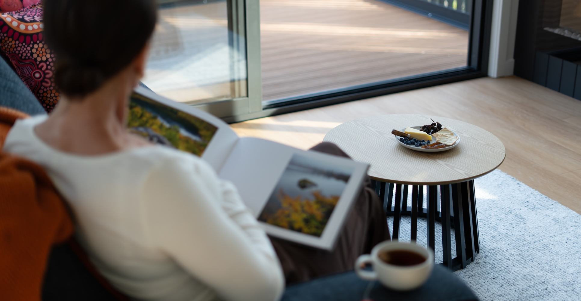 Person reading a book with tea and cheese board on coffee table