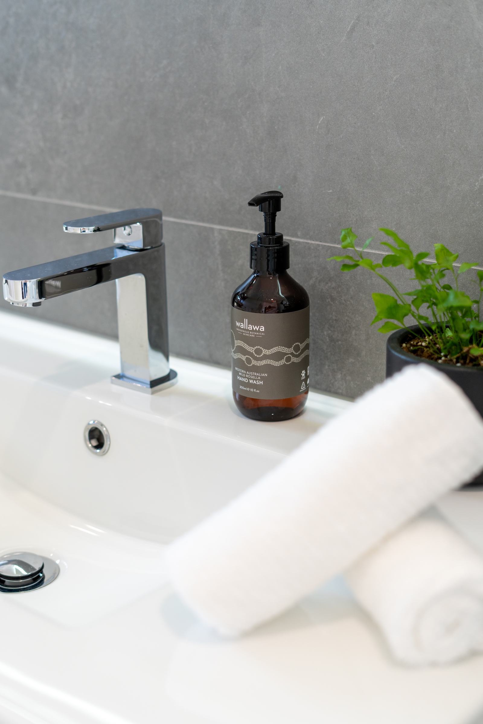 Plush cotton towels on sink with soap and indoor plant