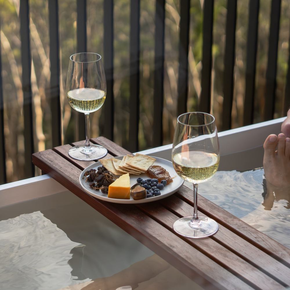 Two people in outdoor bath enjoying wine and cheese board
