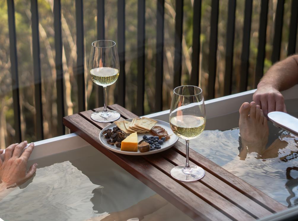 Two people in outdoor bath enjoying wine and cheese board
