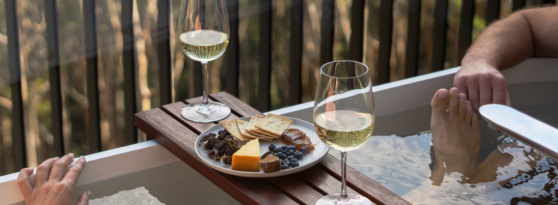 Two people in outdoor bath enjoying wine and cheese board